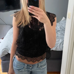 Svart spetsblus - Supersnygg svart blus i spets med vackra volangdetaljer längs ärmar och nederkant. Blusen är ärmlös och har en croppad passform som ger en trendig look. På bilden har jag linne under💗