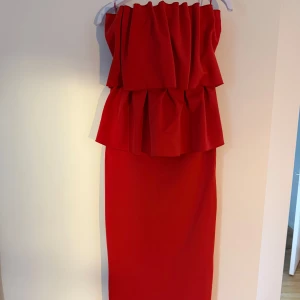 Röd långklänning från Dagmar, stl 36 - Sculpted långklänning från House of Dagmar i intensivt röd färg. Klänningen är axelbandslös med volangdetaljer upptill och har en slits bak. Tillverkad i återvunnen polyester och elastan för en slim passform. 