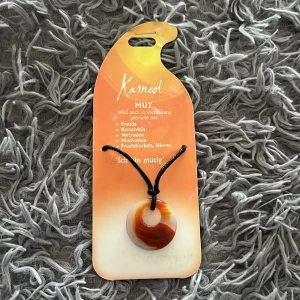 Kristall halsband med svart snöre - Unikt halsband med rund kristall i varma toner av rödbrunt, orange och vitt. Hängs i ett svart snöre som enkelt kan justeras. Stenen har naturliga mönster och ger en cool, bohemisk vibe. Perfekt accessoar för dig som gillar kristaller och personlig stil.