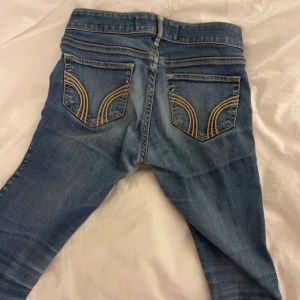  Hollister jeans - Snygga blå jeans från Hollister med klassisk femficksdesign och coola broderade detaljer på bakfickorna. Jeansen har låg midja och är tillverkade i stretchig bomullsdenim. Perfekta till sneakers eller boots.   Pris är diskuterbart!!!