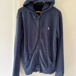 Blå hoodie från Polo Ralph Lauren - Säljer en blå hoodie från Polo Ralph Lauren med dragkedja och huva. Storlek Small men passar även Medium.
