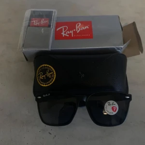 Svarta Ray-Ban Wayfarer solglasögon - Klassiska svarta Ray-Ban Wayfarer solglasögon med polariserade glas. Snygg, tidlös design med fyrkantig form och diskreta silvriga detaljer vid bågarna. Kommer med originalfodral och box. Perfekta för att lyfta din stil i solen.