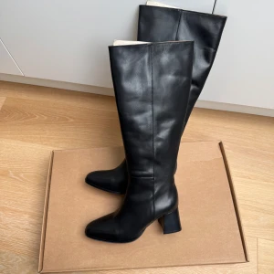 Colette Flattered - Storlek 39. Nypris 4295. Stilrena svarta stövlar i skinn från Colette med medelhög blockklack och spetsig tå. Klassisk design med slät yta och dragkedja på insidan. Perfekta för dig som vill ha en tidlös och elegant look.