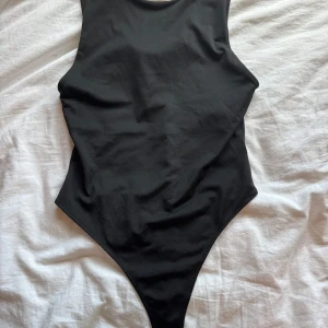 Svart bodysuit från SKØN - Säljer en svart bodysuit från SKØN med hög halsringning och ärmlös design. Bodyn har en clean och tight passform med klassisk siluett, perfekt att styla med jeans eller kjol. Materialet är mjukt och stretchigt för en bekväm känsla hela dagen.