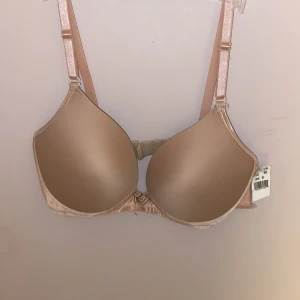 Beige push-up bh med glittriga band - Helt ny.  Nypris 700kr            Snygg beige push-up bh med glittriga axelband och slät kupa. Bh:n har justerbara band och en liten rosett framtill. Perfekt under ljusa toppar för en clean look. Materialet känns mjukt och följsamt mot huden.