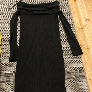 Svart offshoulder klänning Gina Tricot - Snygg svart ribbad klänning från Gina Tricot med offshoulder och långa ärmar. Klänningen är figurnära och har en stilren, enkel design som passar perfekt när du vill känna dig extra cool. Materialet är mjukt och stretchigt för en bekväm känsla.