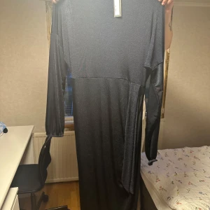Svart långärmad maxiklänning - Snygg svart långklänning med lång ärm och enkel, stilren design. Klänningen har en lätt glittrig yta och är i ett mjukt, stretchigt material. Perfekt för dig som gillar minimalistisk och elegant stil.OBS köparen står för fraktkostnaden