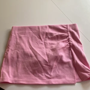 Rosa minikjol från Bershka - Priset kan sänkas!! Supersöt rosa minikjol med inbyggda shorts från Bershka i mjuk bomull. Kjolen har en enkel design med liten slits på sidan och lätt rynk vid midjan. Perfekt för dig som gillar en clean och feminin stil. Använd cirka 3 gånger.