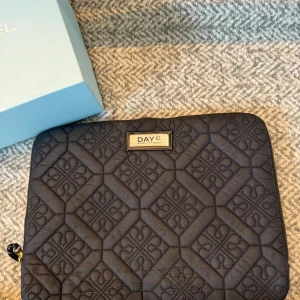 svart datorväska från DAY ET - Säljer en stilren svart quiltad datorväska från DAY ET. Väskan har ett snyggt geometriskt mönster och guldig dragkedja. Perfekt för att bära din laptop med lite extra stil och skydd. Klassisk design som funkar till allt. Den är samma storlek som min MacBook. Nypris 600
