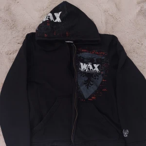 Svart hoodiejacka från WAX, S - Svart hoodiejacka från WAX med dragkedja, tryck på både fram- och baksida samt huva. Snygga vita och röda detaljer och ett stort motiv på ryggen. Jackan har kängurufickor och är perfekt för dig som gillar streetwear med attityd. Vill tilläggas att !!DRAGKEDJAN ÄR TRASIG OCH GÅR INTE ATT STÄNGA!! hör av er vid frågor