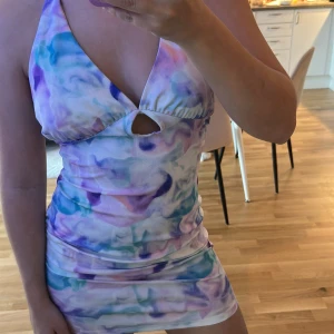 Halterneck miniklänning - Kort klänning med halterneck och knyt i nacken. Mönstret är i pastelliga toner av lila, blått och rosa på vit botten. Klänningen har en liten cut-out framtill och är figurnära med öppen rygg. 