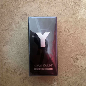Yves Saint Laurent Y Eau de Toilette - Yves Saint Laurent Y Eau de Toilette i en snygg svart och silverfärgad kartong med stor Y-logga framtill. Parfymen kommer i en rektangulär förpackning av kartong och plast, stilren och modern design. Perfekt för dig som gillar exklusiva dofter.