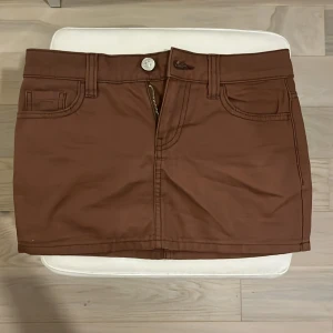 Brun kortkjol från H&M Divided - Snygg brun kortkjol från H&M Divided i bomull. Kjolen har klassisk jeansstil med fram- och bakfickor, bälteshällor och dragkedja framtill. Perfekt för dig som gillar en enkel men trendig look.