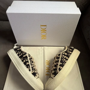 Dior sneakers  - Snygga Dior sneakers med beige och svart monogrammönster, klassisk snörning och robust vit sula. Skorna har tydlig Christian Dior-logga framtill och på hälen. Ovandelen är i textil med exklusiv känsla och detaljer i beige. Perfekta för dig som vill sticka ut.
