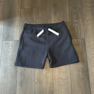 Svarta mjukisshorts med snörning - Svarta mjukisshorts från Russemerch med vit snörning i midjan och fickor på sidorna samt en bakficka. Perfekta för chill eller träning, i mjukt och skönt bomullsmaterial. Klassisk loose.