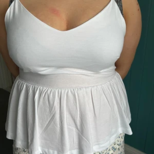 Vit linnetopp från Anna Field Petite - Supersöt vit linnetopp från Anna Field Petite med v-ringad fram- och baksida, bred midjeresår och volangig nederdel. Tunt och mjukt bomullstyg, perfekt för varma dagar. Smala axelband och luftig passform ger en chill och feminin vibe.