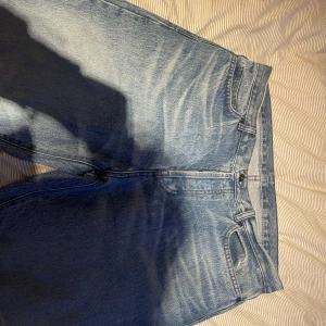 Ljusblå jeans från Lacoste - Säljer ett par ljusblå jeans från Lacoste med klassisk femficksdesign och det ikoniska krokodilmärket på bakfickan. Jeansen har normal passform och är tillverkade i bomullsdenim. Perfekta för en chill och stilren look.