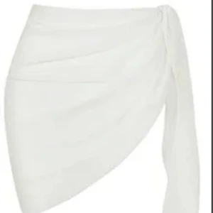 Vit omlottkjol med knyt - Snygg vit kort omlottkjol med knyt i sidan. Kjolen har en asymmetrisk form och är gjord i ett lätt, tunt material som ger en luftig känsla. Perfekt att använd som cover up på stranden. 