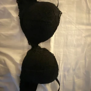 Svart spetsig bh H&M 75B - Svart bh från H&M i storlek 75B. Bh kuporna är täckta med snygg spets och har vaddering för extra form. Axelbanden är justerbara och kanten har fina spetsdetaljer. Perfekt för U och/eller V-ringade tröjor .