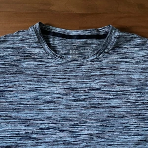 Gråmelerad kortärmad t-shirt - Gym tröja Snygg gråmelerad t-shirt med korta ärmar och rund hals. T-shirten har ett diskret, horisontellt mönster i svart och grått som ger en modern vibe. Perfekt till jeans eller shorts för en chill look.