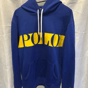 Blå hoodie från Polo Ralph Lauren - Blå hoodie från Polo Ralph Lauren med stor gul logga över bröstet. Lite knottrig annars väldigt bra skick 