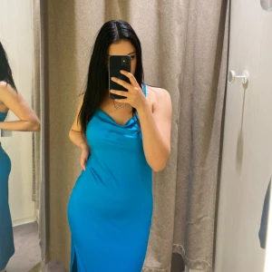 Blå långklänning med slits - Säljer en snygg blå långklänning med tunna axelband och draperad urringning. Klänningen har en slits på sidan som ger en extra touch. Materialet känns mjukt och följsamt, perfekt för sommarkvällar eller när du vill sticka ut lite extra. Aldrig använt!