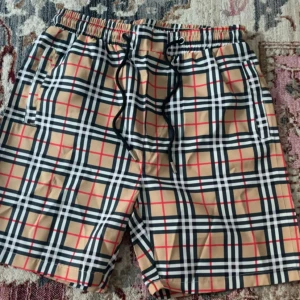 Rutig Burberry shorts med snörning - Snygga shorts från Burberry i klassiskt beige, svart, vitt och rött rutmönster. Modellen har elastisk midja med svart snörning och sidofickor. Perfekta för sommaren och ger en clean, trendig vibe. Materialet känns lätt och passar chill dagar.
