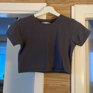 Mörkgrå croppad topp Pull&Bear - En stilren mörkgrå croppad topp från Pull&Bear med rund halsringning och korta ärmar. Enkel och clean design som är lätt att matcha med olika outfits. Perfekt för dig som gillar en basic men trendig look.