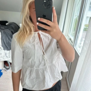 Vit blus med knyt och volang - Söt vit blus med knyt framtill och volang nedtill. Modellen har en lös passform och halvlånga ärmar. Perfekt för en fräsch och avslappnad look. Tillverkad i lätt bomull som känns luftig och skön🥂💗🍉☀️
