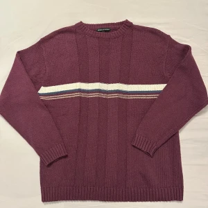 Vinröd stickad tröja Frank & Friends - Vinröd stickad tröja från Frank & Friends med horisontella ränder i vitt, blått och beige över bröstet. Tröjan har rund hals, ribbade muddar och är tillverkad i 100% bomull. Perfekt för dig som gillar en klassisk men ändå chill look.