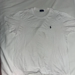 Vit t-shirt från Polo Ralph Lauren - Klassisk vit t-shirt från Polo Ralph Lauren med broderad marinblå logga på bröstet. T-shirten har rund halsringning och korta ärmar. Tillverkad i mjuk bomull som är skön att bära hela dagen.