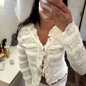Vit spetsblus med volanger och knyt - Superfin vit blus i spets med volangdetaljer och knyt framtill.