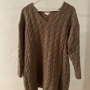 Brun kabelstickad tröja med v-ringning - Mysig brun kabelstickad tröja med v-ringad hals och lång ärm. Tröjan är lång och har en oversized passform 