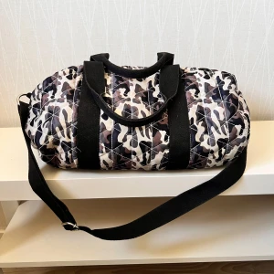 Quiltad camo träningsväska med axelrem - Säljer en quiltad träningsväska med camouflagemönster i svart, beige och brunt. Väskan har både handtag och justerbar axelrem i svart tyg samt dragkedja upptill. Perfekt storlek för gymmet eller sportaktiviteter.