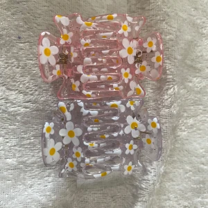 Färgglada hårklämmor med blommor - Säljer ett set med sex hårklämmor i olika färger: rosa, lila, gul, orange och blå. Alla klämmor är dekorerade med vita och gula prästkragsblommor för en söt och somrig vibe. Perfekta accessoarer för att piffa upp frisyren med en lekfull touch. Pris 29kr/2par/bild 