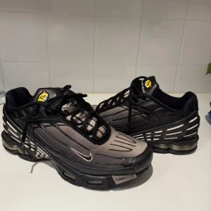 TN skor - Nike Air Max Plus Tuned Air sneakers i svart och grått med coola detaljer och reflekterande inslag. Skorna har en sportig vibe, synlig luftdämpning i sulan och klassisk snörning. Perfekta för dig som gillar streetwear och vill sticka ut.