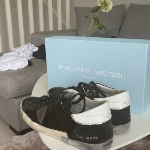Philippe Model svarta sneakers - Snygga svarta sneakers från Philippe Model med vita detaljer och svart snörning med vit text på. Skorna har en klassisk låg siluett, rund tå och är tillverkade i en mix av skinn och mocka.  Köpta från merchsweden för 2999kr för ca 2 månader sedan. Priset är inte hugget i sten, buda på