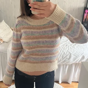 Randig pastellfärgad stickad tröja - Supermysig stickad tröja med pastellfärgade ränder i beige, lila, grön och rosa. Tröjan har rund halsringning, ribbade muddar och lång ärm💕