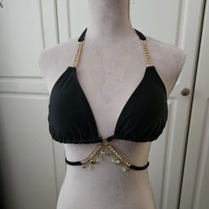Svart bikiniöverdel nytt moda-minx - Supersnygg oanvänd Svart bikiniöverdel med dekorativa detaljer. Den har guldfärgade kedjor med strass på axelbanden och hängen med snäckor och sjöstjärnor framtill. Nypris 499 kr