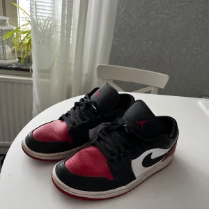 Nike Air Jordan 1 Low - Nike Air Jordan 1 Low i klassisk svart, röd och vit färg. Skorna har svart snörning, röd tåbox och häl, vit sidopanel med svart swoosh och Air Jordan-logga på hälen. Ovandel i skinn och låg profil. Perfekta för dig som gillar streetstyle.