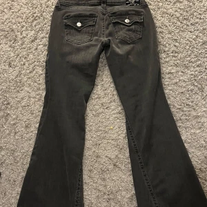 True Religion Joey Low Rise Flare jeans - Svarta jeans från True Religion, modell Joey Low Rise Flare. Snygg bootcut med låg midja och utställda ben. Jeansen har coola bakfickor med lock och silverfärgade knappar samt tydliga kontrastsömmar. Perfekta för dig som gillar en retro vibe. Pris kan diskuteras💗