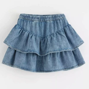 Blå jeanskjol med volanger - Helt ny prislapp kvar!! Supersöt blå jeanskjol med två lager volanger och resår i midjan. Kjolen har en klassisk denimlook och är perfekt för dig som gillar en avslappnad men trendig stil. Passar lika bra till sneakers som boots. Den är i barnstorlekar men passar mig som har XS