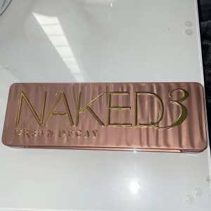 Urban Decay Naked3 ögonskuggspalett - Oanvänd Urban Decay Naked3 ögonskuggspalett med 12 nyanser i rosétoner med både matta och skimriga skuggor. Paletten har en spegel i locket och en dubbeländad borste. Perfekt för att skapa allt från soft glam till mer intensiva looks.  Ordinariepris: 700kr