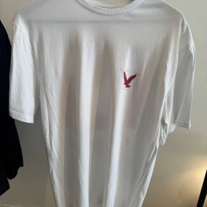 Vit Bagouze oversize t-shirt med röd print - Vit t-shirt från Bagouze med stor röd och vit mås-illustration på ryggen och mindre logga på bröstet. Klassisk passform och rund halsringning, tillverkad i mjuk bomull. Perfekt för dig som gillar streetwear med grafiska tryck.