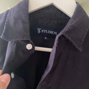 Marinblå Linneskjorta - Snygg marinkblå linneskjorta från St Studios i storlek XS. Skjortan har klassisk krage, vita knappar framtill och vid ärmslut samt lång ärm. Perfekt för dig som gillar stilrena och enkla plagg med en clean look. Har precis den passform man söker i en skjorta och passar för de mellan 168-175. Nu pris 699