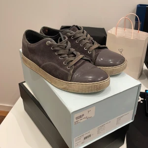 Lanvins - Snygga grå sneakers från Lanvin med ovandel i mocka och tåparti i blankt skinn. Klassisk rund tå, snörning och beige sula ger en stilren vibe. Perfekta för dig som gillar exklusiva och tidlösa sneakers med en twist.