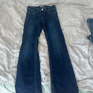Blå bootcut jeans från Gina Tricot - Mörkblå jeans från Gina Tricot med bootcut-modell och kontrastsömmar. Klassisk femficksdesign och snygga detaljer på bakfickorna. Perfekta för dig som gillar en retro vibe och vill ha ett par jeans med lite extra sväng i benen.
