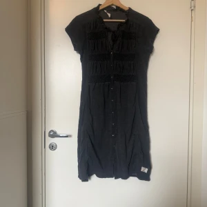 Mörkgrå klänning Odd Molly, strl 2 - Superskön mörkgrå klänning med korta ärmar, knappar framtill och snygga smockdetaljer över bröstet. Liten volang vid halsen och knytband. Perfekt till sneakers eller boots! Från märket Odd Molly i storlek 2 som enligt deras storleksguide motsvarar en storlek M. Fint skick, men tyvärr är den blekare än ny. Kan vara något tvätt påverkad. 