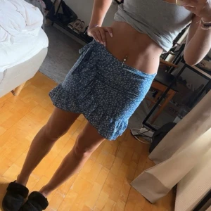 Blå blommig omlottkjol med volang - Säljer då den är för liten för mig, vilket man ser på första bilden. Kjolen har omlottmodell med knyt i sidan och dragkedja bak. Perfekt för sommarens alla dagar, lätt och luftig i materialet.