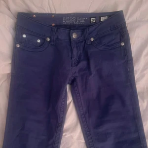 Blå skinny jeans från Miss Me, stl 28 - Säljer ett par blå skinny jeans från Miss Me i storlek 28. Jeansen har snygga detaljer med broderi och bling på bakfickorna samt silverfärgade nitar och knappar. Modellen är tight och sitter snyggt längs benen. Perfekta för dig som gillar statement-jeans!